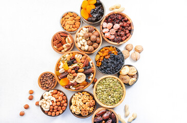 Obraz na płótnie Canvas Dried fruits nuts in bowls set. Dry apricots, figs, raisins, walnuts, almonds and other. Healthy nutritious snacks. White table background, top view, copy space