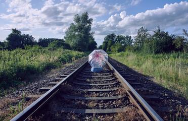Rear view of a woman holding umbrella and sitting on train tracks