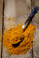 Ground turmeric on a wooden background. A spoonful of turmeric is on the table. Traditional spices.