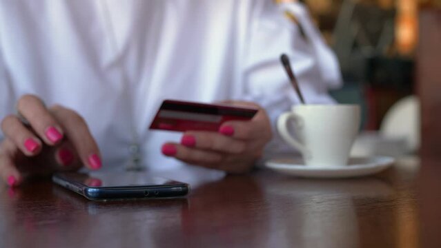 Unrecognizable young woman sitting at home using her credit card for an online order on the mobile phone