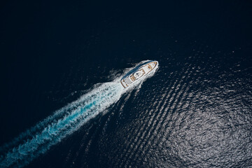 Luxury white mega yacht fast movement on dark water in the ocean top view. Big yacht in the sea drone view. Big white super boat moves on the water leaving a white trail aerial view.