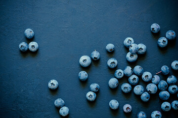 Freshly picked ripe blueberries, scattered on a black textured desk surface. Flat lay background.