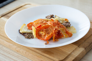 Juicy meat with potatoes, tomatoes and cheese is in the oven, closeup
