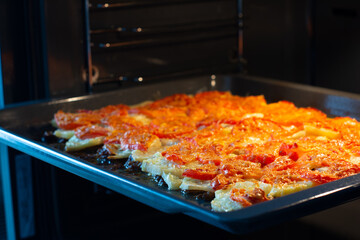 Juicy meat with potatoes, tomatoes and cheese is in the oven, closeup