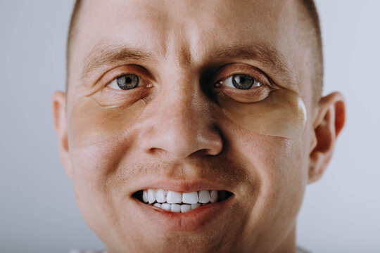 Close-up portrait of a handsome guy with golden gel under the blindfolds applied to his face, looking at the camera, posing against a gray background. Skin care concept. Foreground - Powered by Adobe