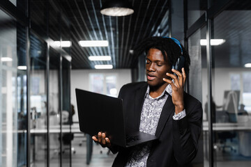 Cheerful black man in headphones listen audio podcast and enjoy music. Handsome african man with laptop in the office. Party concept.