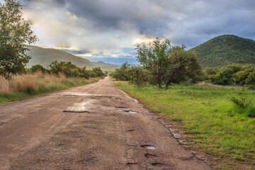 Fototapeta premium A wet Landscape view of mountains, brown and green savanna grassland covered in water drops and rain puddles after a rainstorm, Pilanesburg Nature Reserve, North West Province, South Africa