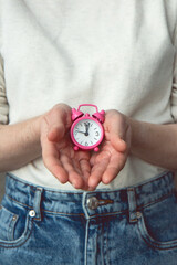 Pink alarm clock in female hands. Time is in our hands. Time concept