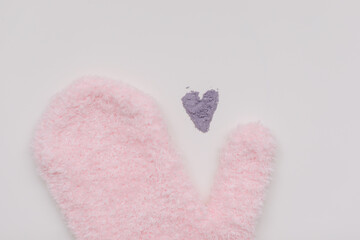 Minimal flat lay composition of massage mitten washcloth and a heart made of violet powder on a white background. Concept of zero waste