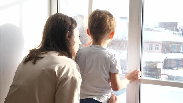 Loving young mother and charming son look out the window from home. The concept of love, family happiness, Valentine's day