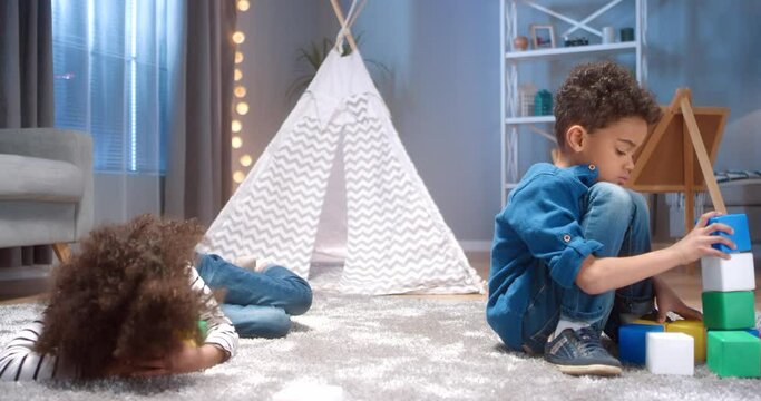 Little African-American girl with the curls resentful and greedily covers the toys while her brother is docile playing alone.