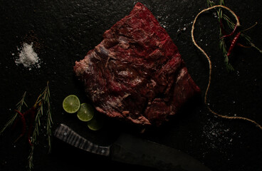 corte de res SHORT RIBS  sobre laja de piedra  con decoración como sal, pimienta limón, chile de árbol  , romero y un cuchillo  