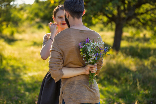 man hides a bouquet behind his back when meeting his girlfriend in the park
