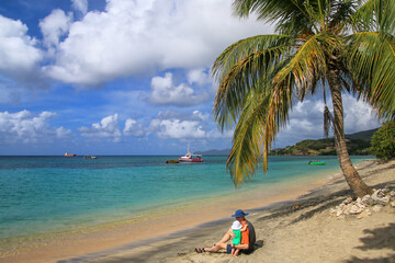 A man with a baby girl sitting at the beach at Hillsborough Bay, Carriacou Island, Grenada. - obrazy, fototapety, plakaty