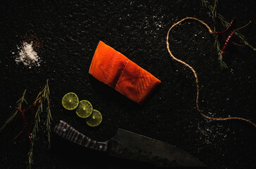 salmón crudo sobre laja de piedra  con decoración como sal, pimienta limón, chile de árbol  , romero y un cuchillo  