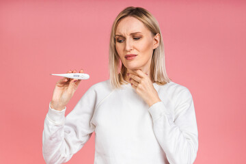 Young woman having flu taking thermometer. Isolated over pink background. Beautiful young woman is...