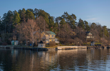 Naklejka premium Old summer houses at the waterfront with a jetty on a cliff at an island a sunny afternoon in the archipelago of Stockholm
