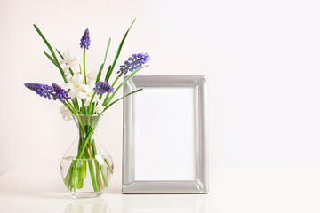 Beautiful flowers bouquet in glass vase and empty photo frame on the table. Muscari and white hyacinth. Mock-up for design.
