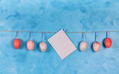 easter eggs and blank paper for label hanging on a blue wooden background with space
