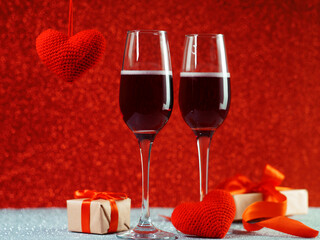 Two glasses of champagne or sparkling wine on a red bokeh background. Gift boxes with red ribbon. The concept of a holiday, Valentine's day or anniversary