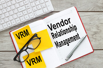 VRM - Vendor Relationship Management open red notepad on desktop near yellow stickers and glasses