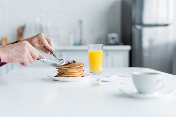 partial view of mam cutting pancakes near orange juice and blurred coffee cup.
