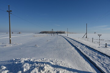 The railway goes into the distance towards the forest on a frosty sunny day.