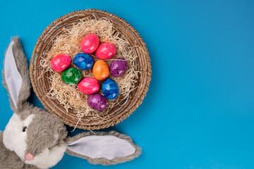Fototapeta na wymiar Easter bunny with colored eggs in a basket on a blue background. Easter concept. Copy space