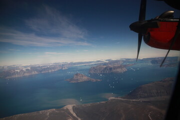 wybrzeże grenlandii z dużej wysokości i śmigło małego czerwonego samolotu widziane przez okno kabiny pilota - 482907710
