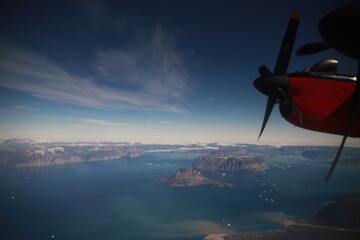 wybrzeże grenlandii z dużej wysokości i śmigło małego czerwonego samolotu widziane przez okno kabiny pilota - obrazy, fototapety, plakaty