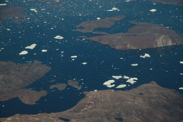 poszarpane surowe i skaliste wybrzeże Grenlandii oraz morze pokryte krą lodową widziane z samolotu z dużej wysokości