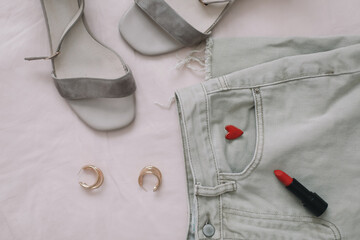 Jeans, sandals and red lipstick on beige background. Overhead view of woman's casual spring summer outfit. Trendy stylish women clothes. Flat lay, top view