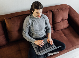 Work from home, home office. A young guy in casual clothes is using laptop for online...