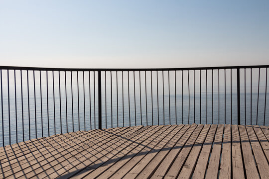 Beautiful wooden terrace with a metal fence is on the beach by the blue sea