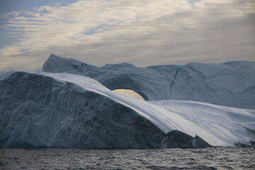 majestatyczna góra lodowa u wybrzeży grenlandii z naturalnie powstałym w niej odłamem w kształcie łuku - obrazy, fototapety, plakaty