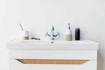 white sink with faucet, dispenser with liquid soap, shaving foam, safety razor and toothbrush.