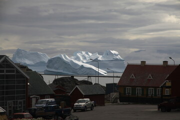 małe czerwone domki w miasteczku u wybrzeży grenlandii oraz morze arktyczne z górami lodowymi i krą w tle - 482909370
