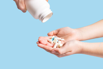 Eating a lot of drugs. Pills from plastic container. Tablets in hand on blue background.