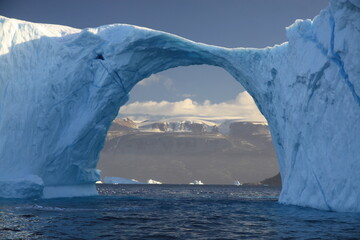 dziura w górze lodowej w kształcie łuku na morzu pokrytym krą w słoneczny dzień - obrazy, fototapety, plakaty