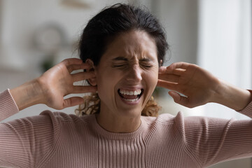 Screaming angry Latin woman cover plug up with fingers ears annoyed by noisy neighbors, unable to hear loud music, unpleasant sound, frown face expression, close up, hysterics, noise, earache concept