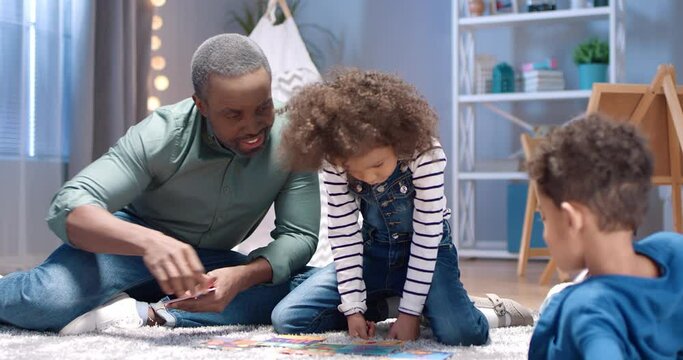 Caring African-American grandfather spends weekend with two grandchildren playing interesting interactive board game. Concept of family leisure for two generations.