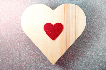 Red glitter heart and wooden one over a silver glitter background