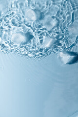 Ice cubes with water drops scattered on a blue background, top view.
