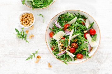 Fresh vegetable salad with arugula, tomato, onion, parmesan cheese and cashew nuts. Top view