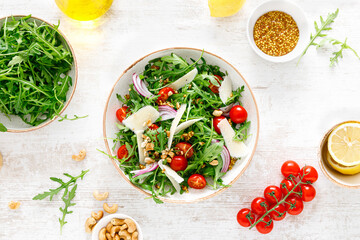 Fresh vegetable salad with arugula, tomato, onion, parmesan cheese and cashew nuts. Top view