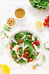 Fresh vegetable salad with arugula, tomato, onion, parmesan cheese and cashew nuts. Top view
