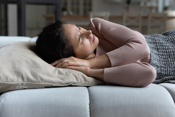 Woman suffer from restless sleep, having insomnia or nightmares, frowning lying on sofa with closed...