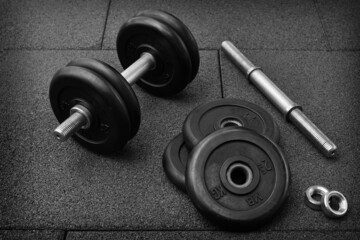 Fototapeta na wymiar dumbbell and iron plates on the rubber floor in the gym. black and white photography. Bodybuilding equipment. Fitness or bodybuilding concept background.