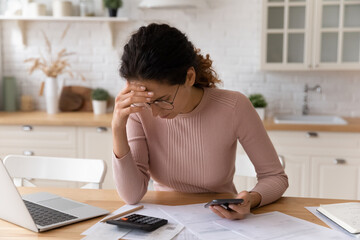 Latina woman sit in kitchen check personal finances, calculate domestic bills feels stressed, think...