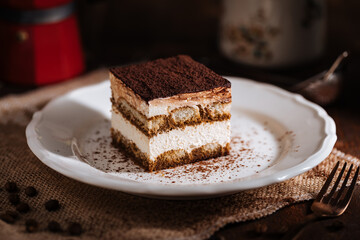 Tiramisu cake dessert served with coffee, biscuit and cocoa as ingredients on a bright white background. One piece